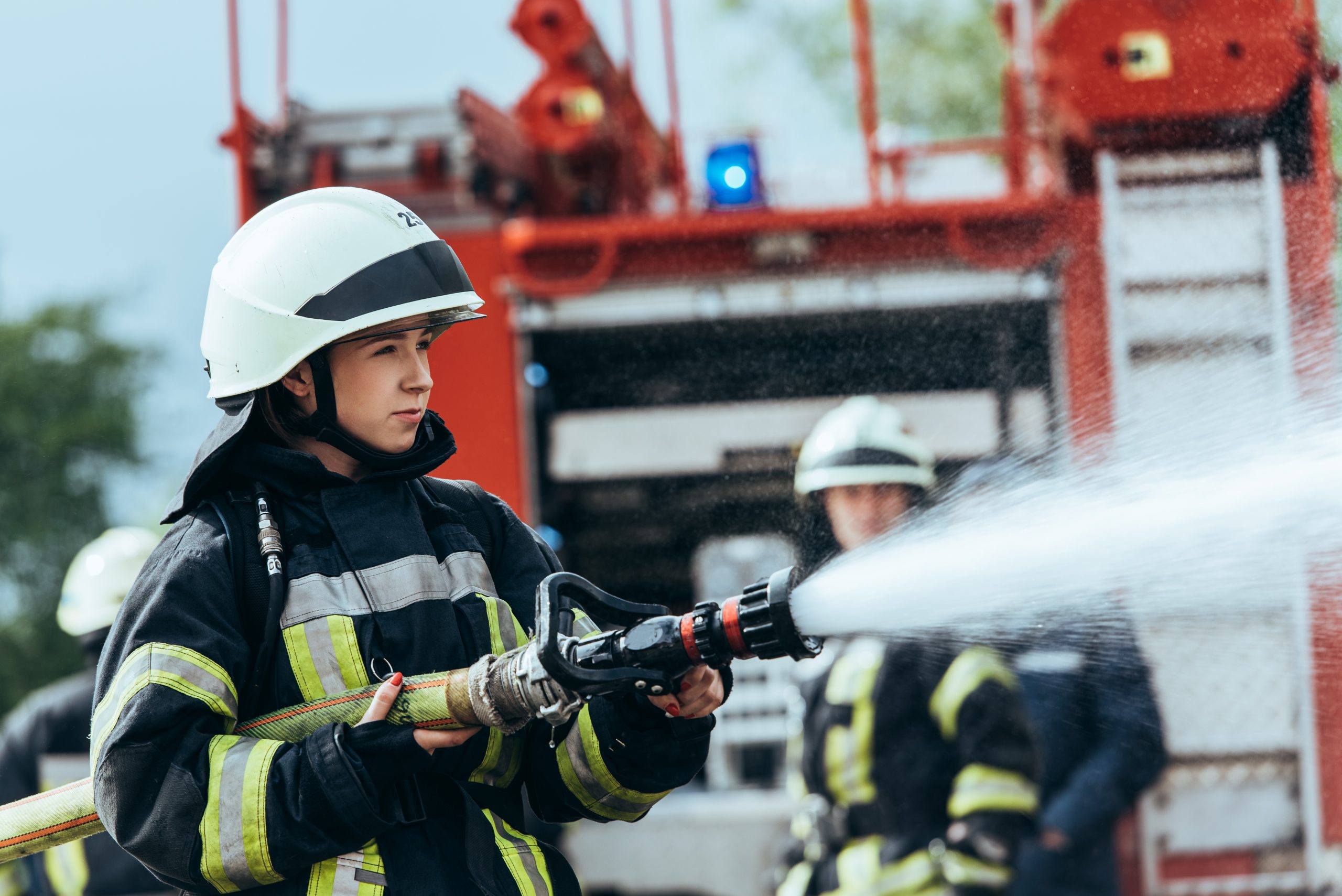female firefighter with water hose extinguishing fire on street