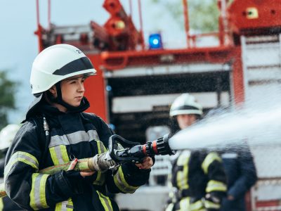 female firefighter with water hose extinguishing fire on street